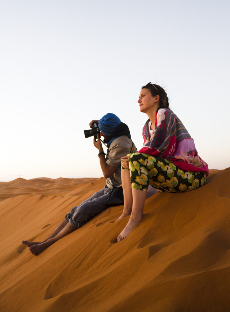 two people sitting top dune taking photos